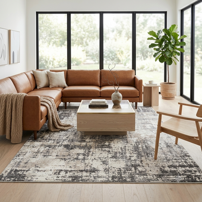 A modern living room featuring a brown leather sectional sofa, a distressed gray and beige patterned area rug, a light wood coffee table, and a large potted fiddle-leaf fig plant by tall black-framed windows.