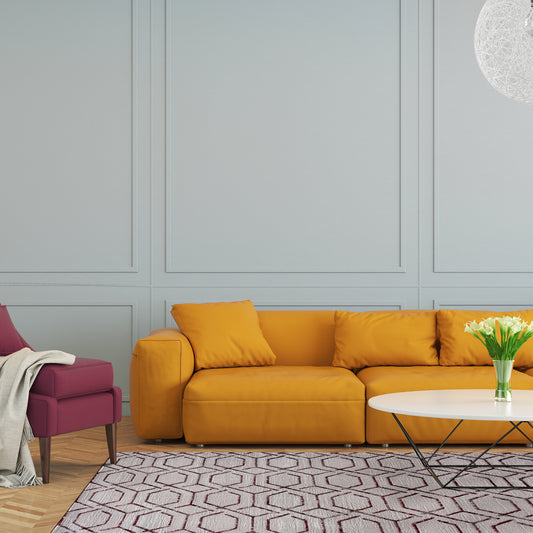 Pera Trellis Rug in a modern formal living room with grey panelled walls, mustard large sofa, burgundy armchair and white coffee table with daffodils on