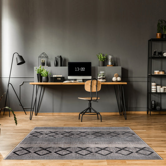 Modern minimalist dark grey home office with grey wall, wooden desk and chair, black floor lamp and Smyrna Midnight Rug